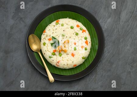 UPMA aus Samolina oder rava Upma, dem berühmtesten südindischen Frühstückselement, das wunderschön auf einem Teller mit Bananenblatt angeordnet und mit einem garnierten Blätterteller serviert wird Stockfoto