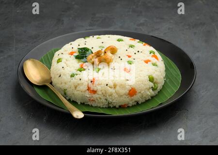 UPMA aus Samolina oder rava Upma, dem berühmtesten südindischen Frühstückselement, das wunderschön auf einem Teller mit Bananenblatt angeordnet und mit einem garnierten Blätterteller serviert wird Stockfoto