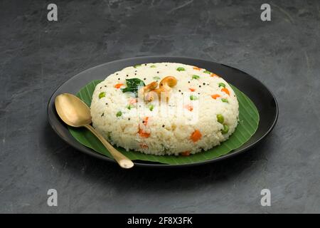 UPMA aus Samolina oder rava Upma, dem berühmtesten südindischen Frühstückselement, das wunderschön auf einem Teller mit Bananenblatt angeordnet und mit einem garnierten Blätterteller serviert wird Stockfoto