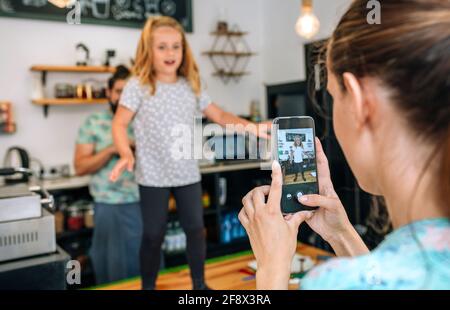 Mutter nahm ihre Tochter auf, die während der Arbeit mit dem Handy tanzte In einem Café Stockfoto