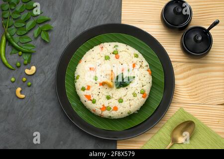 UPMA aus Samolina oder rava Upma, dem berühmtesten südindischen Frühstückselement, das auf einem schwarzen Teller angeordnet ist und mit gebratener Cashewnuss A garniert ist Stockfoto