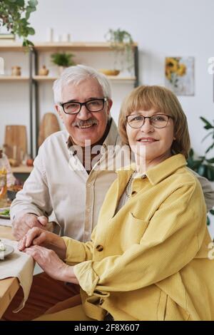 Porträt einer glücklichen älteren Familie von zwei lächelnden Kameralingern Beim Sitzen am Esstisch Stockfoto