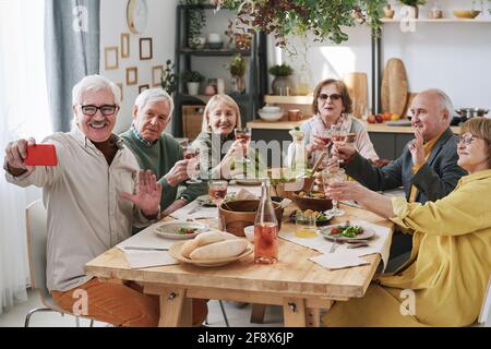 Glücklicher älterer Mann, der sein Mobiltelefon hält und ein Foto macht Mit seinen alten Freunden beim Abendessen am Tisch Stockfoto