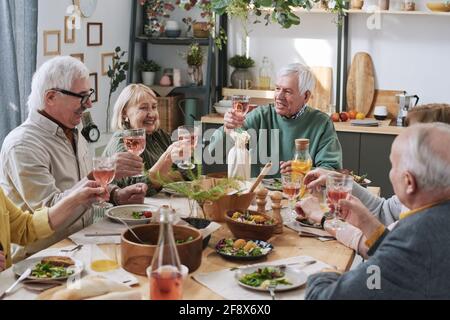 Eine Gruppe glücklicher älterer Menschen, die mit am Tisch sitzen Ein Glas Rotwein und ein Abendessen zu Hause Stockfoto