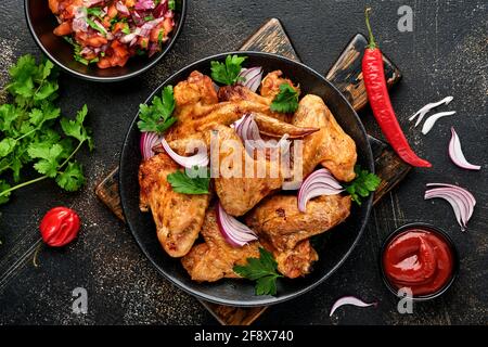 Gegrillte Hähnchenflügel oder gebratener grill mit Gewürzen und Tomatensalsa-Sauce auf einem schwarzen Teller. Draufsicht mit Kopierbereich. Stockfoto