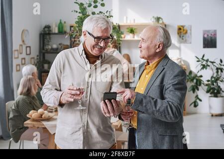 Zwei ältere Männer halten mit dem Handy Gläser Rotwein in der Hand Telefonieren und Online-Arbeit besprechen Stockfoto
