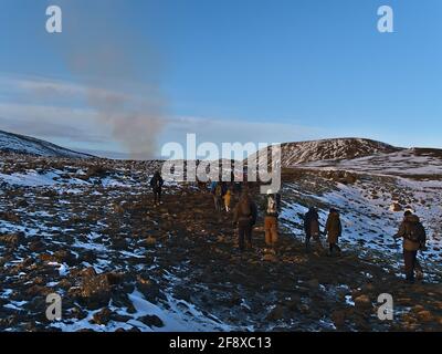 Eine Gruppe von Menschen, die zu einem kürzlich begonnenen Vulkanausbruch am Fagradalsfjall in den Geldingadalir-Tälern wandern, wobei der Vulkan am sonnigen Wintertag rauchig ist. Stockfoto