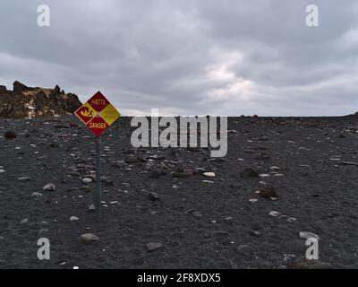 Blick auf den Strand Djupalonssandur an der Küste der Halbinsel Snaefellsnes mit Warnzeichen vor starken Strömungen am bewölkten Wintertag. Stockfoto