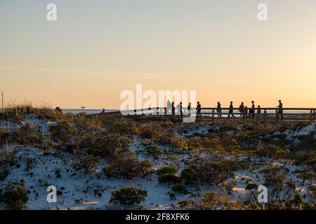 GULF SHORES, AL, USA - 2. APRIL 2021: Silhouetten von Menschen auf der Strandpromenade bei Sonnenuntergang Stockfoto