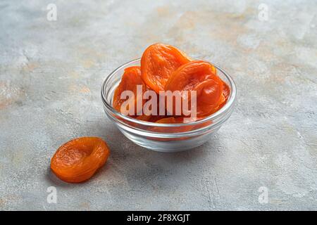 Köstliche getrocknete Aprikosen in einer transparenten Schüssel auf grauem Hintergrund. Gesunde Süßigkeiten. Seitenansicht. Stockfoto