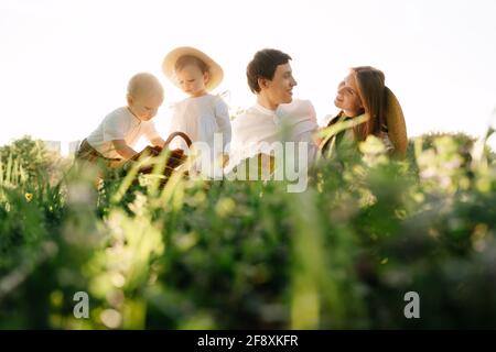 Glückliche Eltern mit Zwillingskindern sitzen auf einem Spaziergang im Park auf dem Gras-Picknick. Stockfoto