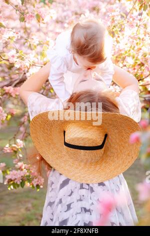 Der Elternteil hält seine Tochter vor dem Hintergrund in den Armen Blühenden Baumes Stockfoto