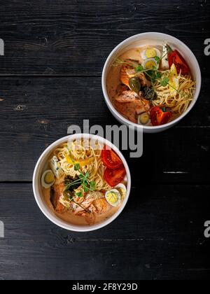 Lachs-Pasta. Appetitliches mediterranes Gericht: Pasta, gebackener Lachs, Tomaten, Kapern und grüne Chilisauce. Köstliche mediterrane Speisen in einer weißen Schüssel Stockfoto