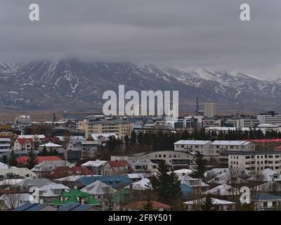 Luftaufnahme des östlichen Teils von Reykjavik mit Wohngebäuden und zerklüfteten, schneebedeckten Bergen, die im Winter in den niedrigen Wolken verschwinden. Stockfoto