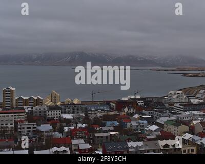 Luftpanorama über die Innenstadt von Reykjavik mit Häusern, Meeresbucht und schneebedeckten Bergen in den niedrigen Wolken im Winter. Stockfoto