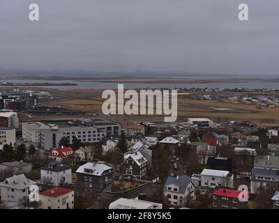 Luftpanorama über den südlichen Teil der Innenstadt von Reykjavik mit Start- und Landebahn des Inlandsflughafens (Reykjavíkurflugvöllur), Gebäuden und Bergen. Stockfoto