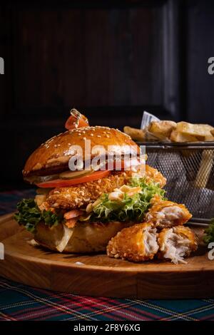 Saftiger Chicken Burger mit frischem Salat und knusprigen pommes frites Auf dem hölzernen Brett - der senkrechte Schuss Stockfoto