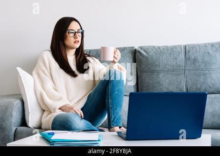 Frau, die zu Hause Kaffee trinkt, während sie mit einem Laptop arbeitet Stockfoto