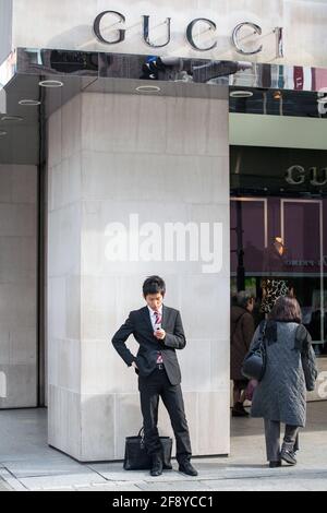 Der japanische Salaryman überprüft das Mobiltelefon, während er vor dem Gucci-Geschäft in Ginza, Tokio, Japan, wartet Stockfoto