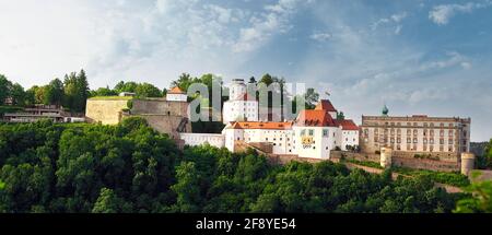 Panoramablick auf die Festung Veste Oberhaus mit Blick auf Passau, Bayern, mit historischen Gebäuden und bewaldeten Hügeln unter blauem Himmel. Stockfoto