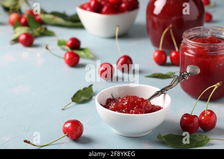 Hausgemachte Süßkirschkonfitüre in einer weißen Schale und Gläser auf hellblauem Hintergrund. Nahaufnahme Stockfoto
