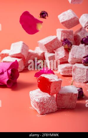 Schwebender rosa türkischer Genuss mit Blütenblättern und Rosengeschmack Trockene Rosenknospen auf rosa Hintergrund Stockfoto