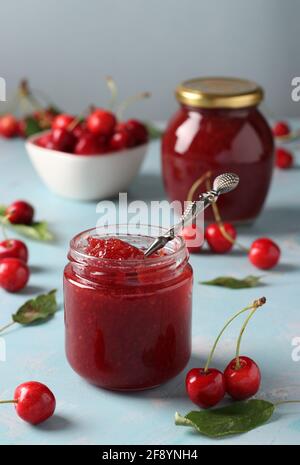 Zwei Gläser hausgemachte Konfitüre aus Süßkirsche auf hellblauem Hintergrund. Vertikales Format Stockfoto