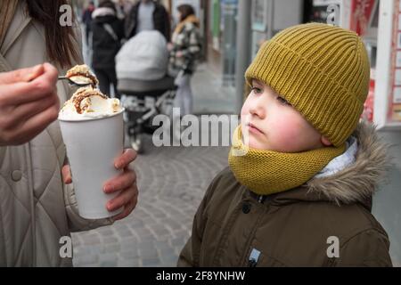 Kleiner Junge, der draußen mit Karamell-Latte und Löffel füttert Stockfoto