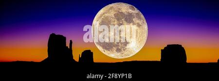 Supermoon bei Sonnenaufgang über Silhouetten von Mitten Buttes und Merrick Butte, Monument Valley, Arizona, USA Stockfoto