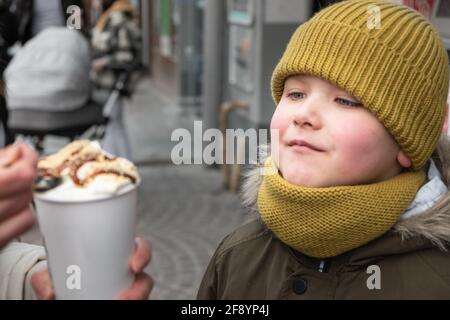 Kleiner Junge, der draußen mit Karamell-Latte und Löffel füttert Stockfoto