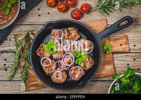 Fleischbällchen mit Feta-Käse in einer gusseisernen Pfanne auf einem rustikalen Holztisch, Draufsicht Stockfoto