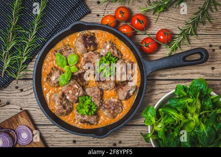 Würzige Fleischbällchen mit Feta-Käse in cremiger Tomatensauce mit Herbes auf einem rustikalen Holztisch, Draufsicht Stockfoto