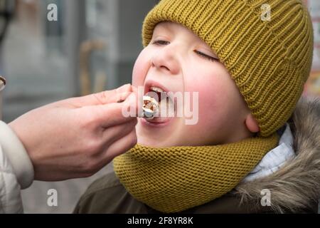 Kleiner Junge, der draußen mit Karamell-Latte und Löffel füttert Stockfoto