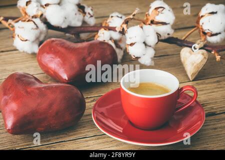 Rote Tasse mit Espresso-Kaffee auf Holz, dekoriert mit roten großen Herzen und einem Baumwollzweig Stockfoto
