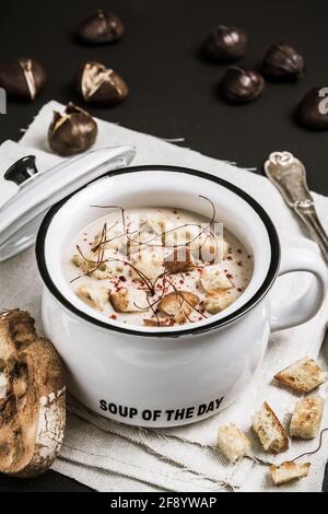 Kastaniensuppe mit Croutons und Chilischoten und Fäden in weißem Keramiktopf auf schwarzem Hintergrund, vertikal Stockfoto