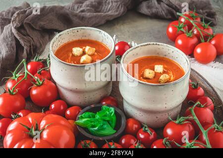 Zwei Tassen gefüllt mit frischer, hausgemachter Tomatensuppe auf einem Holzschale mit einer Vielzahl von reifen Tomaten Stockfoto