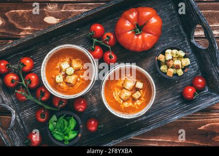Zwei Tassen gefüllt mit frischer hausgemachter Tomatensuppe auf einem Holztablett auf Holzgrund, Draufsicht Stockfoto