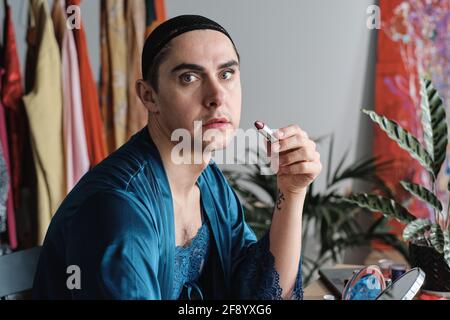 Porträt von Transgender in weiblicher Kleidung, während sie die Kamera betrat Roten Lippenstift auf den Tisch auftragen Stockfoto