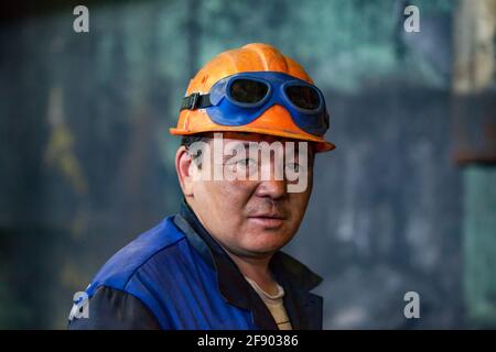 Aksu, Region Pavlodar, Kasachstan. Wärmekraftwerk. Porträt eines erwachsenen asiatischen Arbeiters in orangefarbenem Hardhut. Mit Schweißschutz Stockfoto