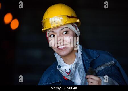 Ekibastuz, Kasachstan - 28. Mai 2012: Porträt einer jungen asiatischen Arbeiterin in gelbem Hardhat. Mit Gesichtsmaske und Brille. Posiert und lächelt. Stockfoto