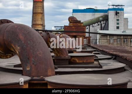 Auf dem Dach des Heizkraftwerks. Alte verrostete Rohre des Belüftungssystems. Industriegebäude sind nicht im Fokus. Blauer Himmel mit Wolken. Karaganda, Kaza Stockfoto