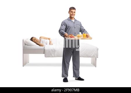 Mann im Schlafanzug trägt ein Frühstückstablett und Frau schläft In einem Bett auf weißem Hintergrund isoliert Stockfoto