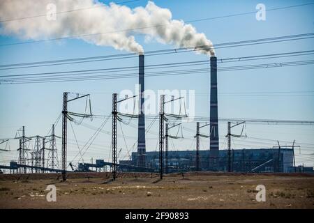 Ekibastuz, Kasachstan. Elektrische Masten im Vordergrund und Elektrizitätswerk mit rauchenden Fabrikschornsteinen (im Hintergrund). Stockfoto