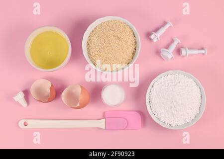 Zutaten für die Herstellung von hausgemachten französischen Macarons-Süßigkeiten, darunter Puderzucker, gemahlene Mandeln, Eiweiß, Salz und Backwerkzeuge auf Rosa Stockfoto