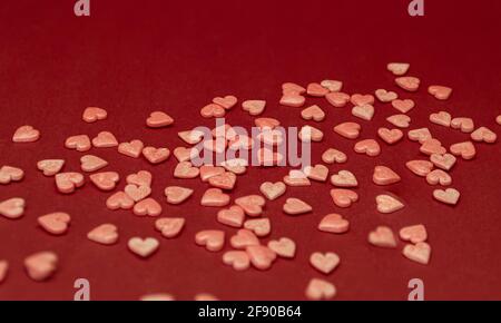 Kleine Zuckerherzen sind über die Oberfläche verstreut. Pinke Herzen auf rotem Hintergrund. Liebeskonzept Stockfoto