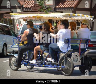 Seitenrückansicht von acht Personen, die mit einem 4-rädrigen Fahrrad fahren, um Spaß und Sightseeing-Freizeittourismus im dänischen Dorf Solvang, CA, USA, zu erleben Stockfoto