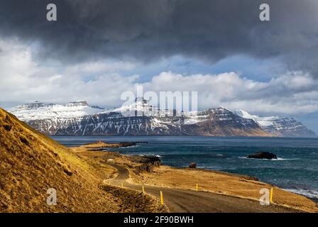 Landschaft mit Küstenstraße und schneebedeckten Bergen im Hintergrund, Island Stockfoto
