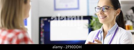 Lächelnder Arzt im Gespräch mit dem Patienten am Tisch in der Klinik Stockfoto