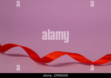 Rotes Satinband Locken auf fliederem Hintergrund, freier Platz. Stockfoto