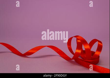 Rotes Satinband Locken auf fliederem Hintergrund, freier Platz. Stockfoto